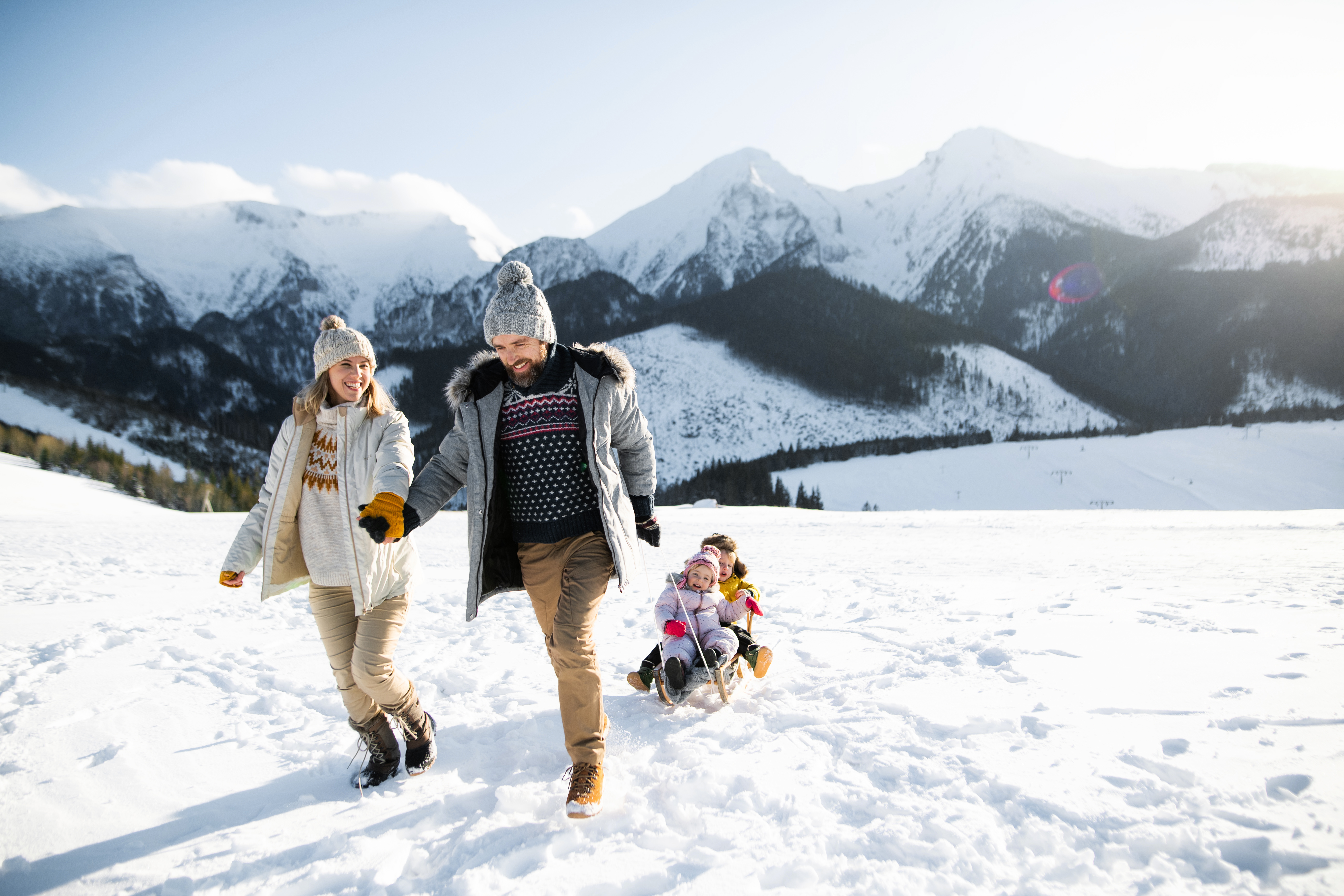 Front view of mother and father pulling son and daughter on sled.